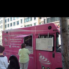 two people standing in front of a pink ice cream truck parked on the side of a street