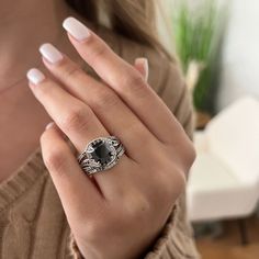 a woman's hand wearing a ring with a black stone on it and white nails