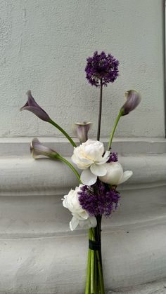 a vase filled with purple and white flowers on top of a stone pillar next to a wall