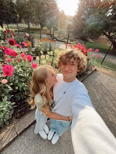 a young man and woman taking a selfie in front of flowers at the park