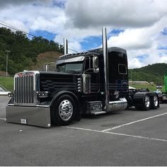 a black semi truck parked in a parking lot next to a green tractor trailer and other vehicles