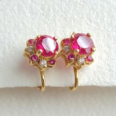 Vintage faux ruby and clear crystal set stone gold electroplated clip on earrings. The earrings have a center pink faux "Ruby" with smaller pink and clear stones around. It has a slightly raised design. They earrings measure appropriately 10mm. They are very well made and in good condition, consistent with age and use. Pink Clip-on Jewelry For Anniversary, Pink Clip-on Earrings For Anniversary, Festive Pink Ruby Earrings, Pink Ruby Dangle Jewelry, Formal Pink Round Clip-on Earrings, Pink Ruby Dangle Earrings, Nickel-free Red Crystal Earrings, Vintage Gold Clip-on Earrings With Rhinestones, Crystal Set