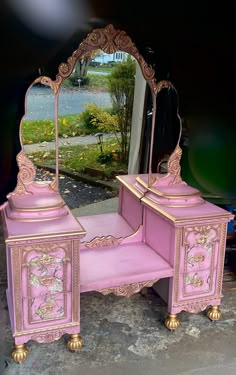 a pink vanity with mirror and gold trimmings on the top, in front of a black background