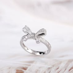 a diamond bow ring sitting on top of a white furnishe background with feathers