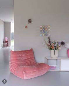 a pink bean bag chair sitting in the middle of a living room next to a vase with flowers