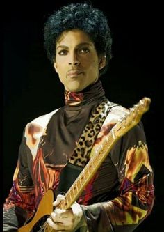 a man with an afro holding a guitar in front of a black background and wearing a leopard print shirt