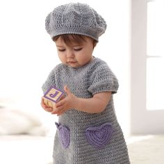 a small child wearing a crochet dress and hat holding a toy in her hands