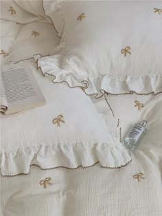 an open book is laying on a bed with white linens and ruffled edges