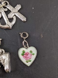 This listing is for 5 different silver tone charms. There is a pair of shoes, enameled heart, heart with rhinestone, anchor and cross. Three match and are on the same ring. The enameled heart is marked Wells Ster. The charms measure 15-20 mm long. They all have some wear including a few small chips of missing finish. R Vintage Metal Heart Charms, Silver Heart Charms With Dangling Details, Vintage Metal Heart Charm, Silver Heart Shaped Dangling Charms, Silver Heart-shaped Dangling Charms, Silver Metal Heart Charm, Silver Heart Charm In Metal, Silver Enamel Heart Charm Jewelry, Silver Enamel Jewelry With Heart Charm