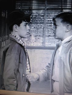 two young men standing next to each other in front of a window with shutters