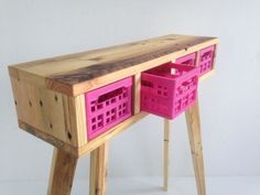 a wooden table with two pink baskets on the top and bottom drawer, in front of a white wall