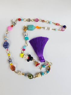 a purple tasseled necklace with charms and beads hanging from it's side