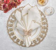 a place setting with napkins, wine glasses and flowers on a tableclothed surface