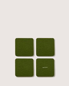 four square green coasters with white lettering on the front and back, set against a gray background