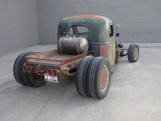 an old green truck parked in a parking lot next to a garage door and wall