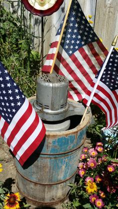 two american flags are placed on top of an old water pump in a garden with wildflowers