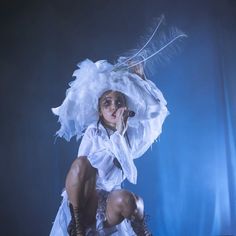 a woman dressed in white with feathers on her head and boots, crouching down