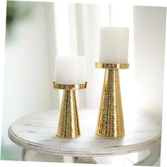 two white candles sitting on top of a table next to each other with gold accents