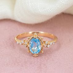 a ring with an oval blue topaz surrounded by small white diamonds on a pink velvet surface