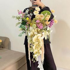 a woman standing in front of a couch holding a bouquet of flowers and taking a selfie