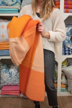 a woman is holding an orange and pink scarf in front of a shelf full of fabrics