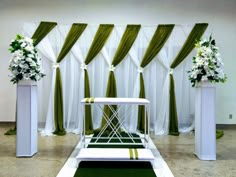 an aisle decorated with white flowers and green drapes