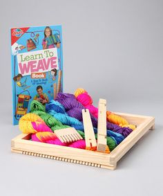 a wooden box filled with yarn next to a book on the cover that says learn to weave