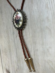 This awesome bolo tie is handmade in our shop, it has a colorful rose cabochon and a brass metal backing and brown leather adjustable cord. Quality guaranteed, picture does not do this buckle justice! We have matching belt buckles to pair! Handmade Festival Bolo Ties, Vintage Brown Jewelry For Rodeo, Handmade Adjustable Bolo Ties For Festivals, Vintage Brown Jewelry For Western-themed Events, Vintage Adjustable Hand Tooled Bolo Tie, Adjustable Vintage Hand Tooled Bolo Tie, Vintage Adjustable Jewelry For Western-themed Events, Retro Adjustable Brown Jewelry, Retro Brown Adjustable Jewelry