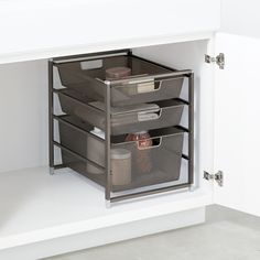 three bins are shown in the corner of a kitchen cabinet with white walls and flooring