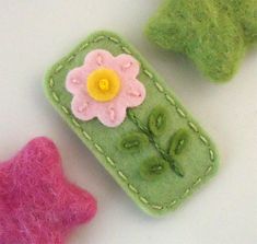 three felt flowers are sitting next to each other on a white surface with two pink and one green flower