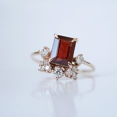 This Bordeaux Garnet ring is fit for a royalty. Featuring a natural garnet surrounded by sparkling white CZs. Handcrafted in your choice of gold vermeil, or 14K solid gold. Gold vermeil or 14K solid gold 8x6mm natural emerald cut garnet stone Round CZs (what's this?) 1.2mm ring band ** This item is specially made for you. Please allow 1-2 week lead time. ShippingDomestic: Free standard shipping within the U.S.International: Free standard shipping for orders over $150 Custom SizesNot sure what yo Red Stone Engagement Rings, Birthstone Engagement Rings, January Birthstone Rings, Make Rings, Red Garnet Ring, American Diamond Jewellery, Gem Ring, Garnet Ring, January Birthstone