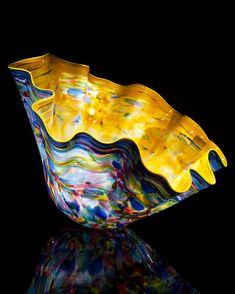 a colorful glass bowl sitting on top of a black surface with its reflection in the water