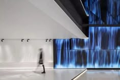 a person walking in front of a wall with blue lights on it and water flowing down the side