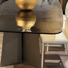 a black table with a gold vase sitting on it's top and white chairs in the background