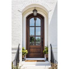 the front door to a white brick house with two potted plants on either side