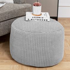 a grey ottoman with a book on top and a plant in the middle sitting on it