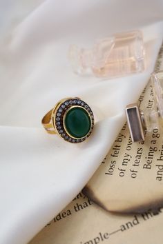 This elegant ring features a central green stone surrounded by sparkling cubic zirconia, adding a touch of glamour to any ensemble. Its versatility makes it perfect for complementing a variety of outfits and styles. Finish: 22KT Gold Plating Material: Silver, Copper Alloy, Polki Color: Green Size: One Size Closure Type: Adjustable Box Contains: 1 Ring Elegant Oval Emerald Ring With Stone Setting, Elegant Round Diamond Ring, Elegant Round Diamond Ring With Stones, Elegant Crystal Open Ring With Stones, Elegant Open Crystal Ring With Stones, Elegant Green Emerald Ring With Round Stone, Green Diamond Open Ring With Center Stone, Elegant Open Crystal Ring, Green Jeweled Round Ring