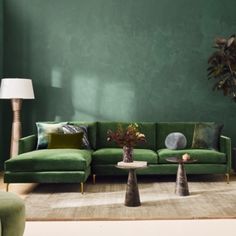 a living room with green couches and pillows on the floor in front of a potted plant