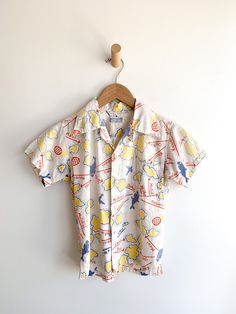 Darling cotton short sleeve Hawaiian Island motif shirt. Beautiful aging and fade. Fabric: CottonLabel: Watumull'sFit: XSEra: 1930/50’s Measurements: Bust 36" Shoulder 14" Sleeve 5.5" Sleeve hole opening (flat) 6" Length 21" Waist 34" Condition: Very good. One small hole on front and a bunch of small paint(?) dots on front (see photos). Pre-washed Short Sleeve Tops For Summer, Collared Cotton Hawaiian Shirt With All-over Print, Cotton Short Sleeve Collared Shirt With All Over Print, White Cotton Hawaiian Shirt With All Over Print, Cotton Hawaiian Shirt With All Over Print, White Cotton Hawaiian Shirt With Print, Patterned Cotton Camp Shirt With Short Sleeves, Retro Collared Short Sleeve Shirt With Graphic Print, Retro Cotton Hawaiian Shirt With Short Sleeves