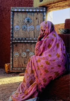 a woman sitting on the ground talking on her cell phone in front of a door