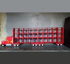 a red toy truck is parked in front of a gray wall with shelves on it