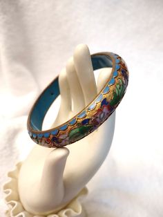 Vintage Chinese Champlevé Cloisonne bangle bracelet.   Flowers and leaves in raised enamel on a gilt base.  Raised enamel blue scalloped edge, rounded outside, flat blue enamel inside.   Older vintage piece (circa 1950s) in excellent condition.   No missing enamel. 1/2 inch wide, ¼  inch thick, 1 1/2 inch, 7 3/4 inch inner circumference. This process is the opposite of the cloisonné technique: instead of building up on the surface of the metal object,  the surface is gouged away, creating trough Blue Enamel Bracelet Jewelry, Vintage Turquoise Enamel Jewelry, Antique Blue Round Bracelets, Blue Enamel Bangle Gift, Blue Enamel Bangle As A Gift, Blue Enamel Bangle Perfect As A Gift, Vintage Blue Enamel Bracelets, Antique Blue Bracelet As Gift, Blue Enamel Bangle Bracelets