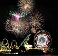 fireworks are lit up in the night sky above amusement rides and ferris wheel at an amusement park