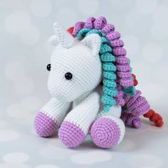 a crocheted stuffed unicorn sitting on top of a white table next to a gray wall