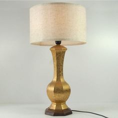 a gold lamp with a white shade on it and a cord plugged into the base