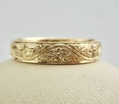 a gold wedding ring sitting on top of a white surface with an intricate design in the middle