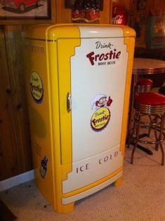 a yellow and white refrigerator sitting in a kitchen next to a table with red chairs