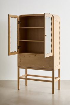 a wooden cabinet sitting on top of a floor next to a white wall with an open door