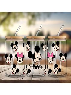 three mickey mouse tumblers with straws in them sitting on a wooden table outside