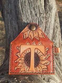 a leather wallet with the letter t on it sitting in front of a tree trunk